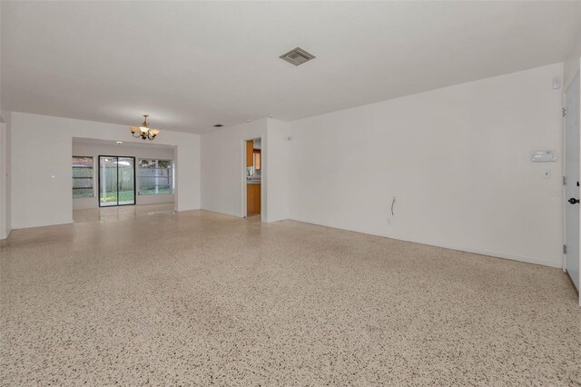 empty room with visible vents, a notable chandelier, and speckled floor