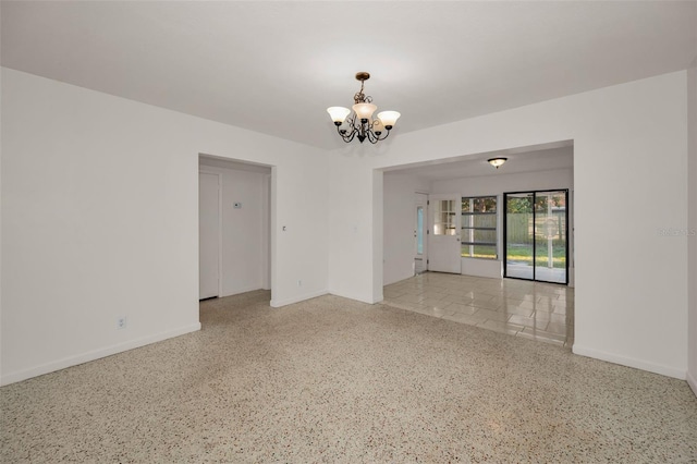 spare room featuring a chandelier, speckled floor, and baseboards