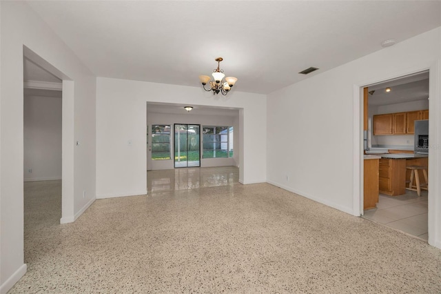 unfurnished room with light speckled floor, visible vents, a notable chandelier, and baseboards