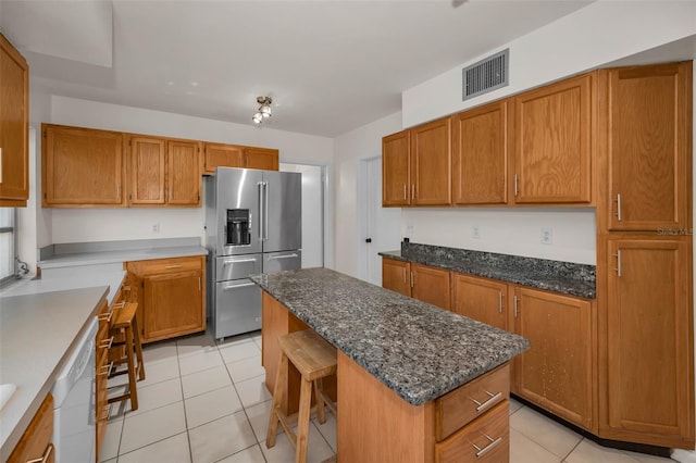 kitchen featuring light tile patterned floors, visible vents, brown cabinets, a center island, and high end fridge