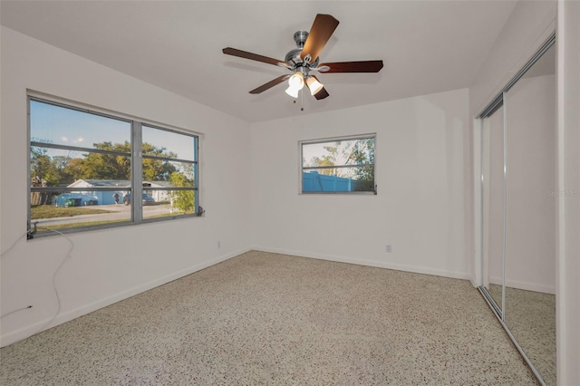 unfurnished bedroom featuring a closet, multiple windows, baseboards, and speckled floor