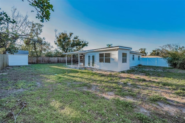 back of property featuring an outbuilding, a fenced backyard, a yard, french doors, and a storage unit