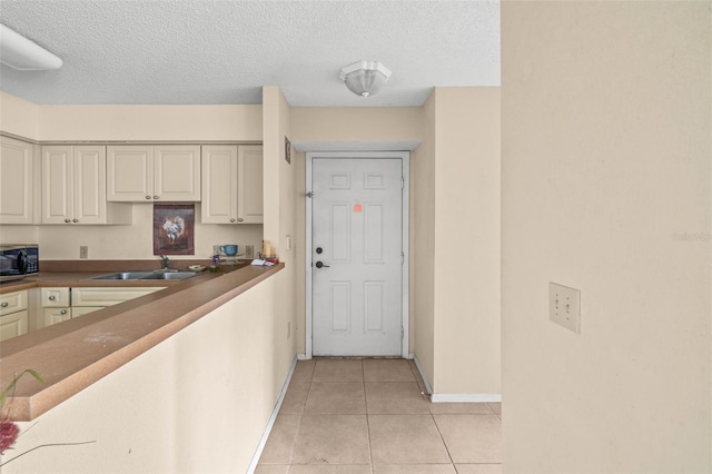 kitchen with black microwave, light tile patterned flooring, a sink, cream cabinetry, and dark countertops