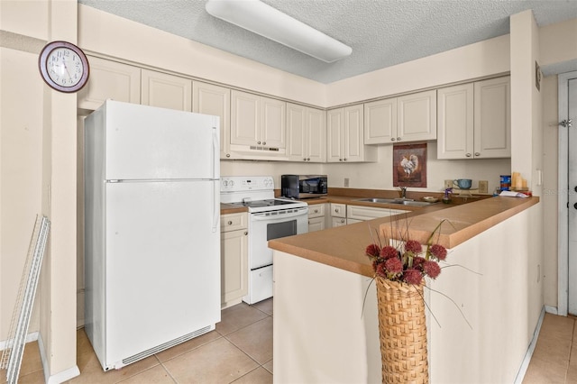 kitchen with a textured ceiling, light tile patterned flooring, a peninsula, white appliances, and a sink