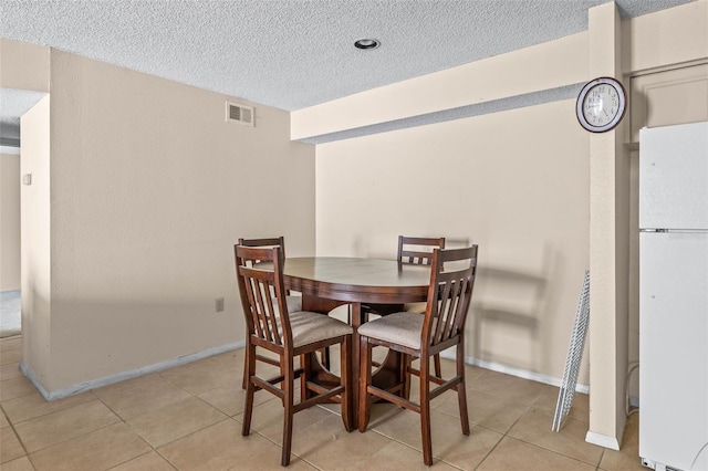 dining area with a textured ceiling, light tile patterned floors, visible vents, and baseboards