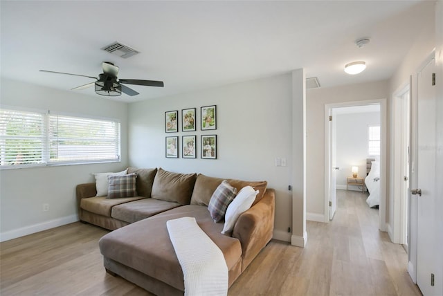 living room featuring visible vents, baseboards, a ceiling fan, and light wood finished floors