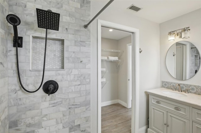 bathroom featuring visible vents, a walk in closet, baseboards, tiled shower, and vanity