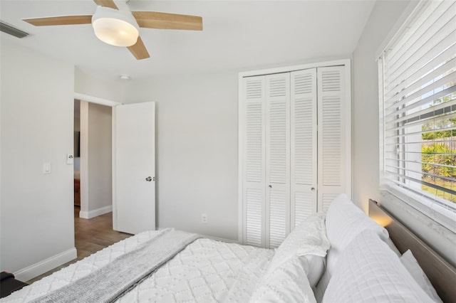 bedroom with visible vents, a ceiling fan, wood finished floors, a closet, and baseboards