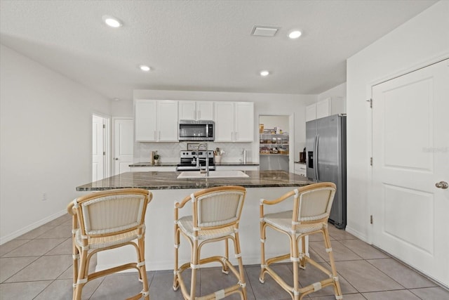 kitchen featuring appliances with stainless steel finishes, white cabinets, light tile patterned floors, and tasteful backsplash