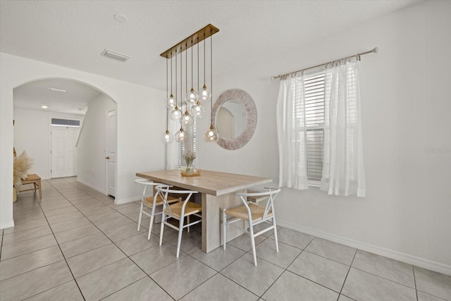 dining room with arched walkways, a textured ceiling, light tile patterned flooring, and baseboards