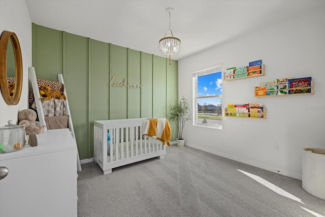 bedroom with a crib, carpet, baseboards, and a notable chandelier