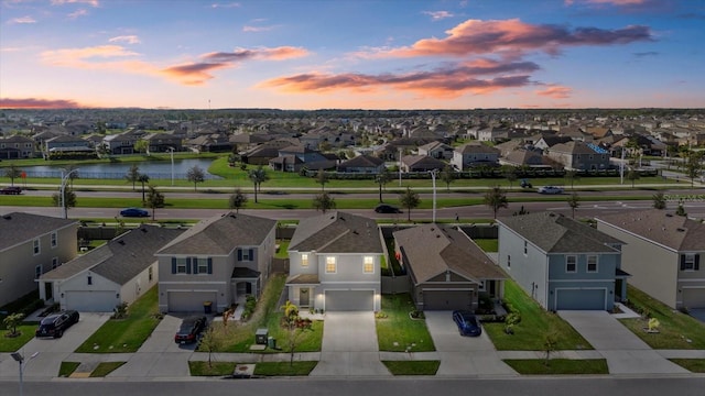 aerial view at dusk with a water view and a residential view