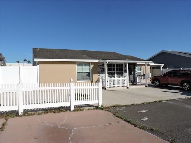 view of front of property with a fenced front yard, concrete driveway, a shingled roof, and stucco siding