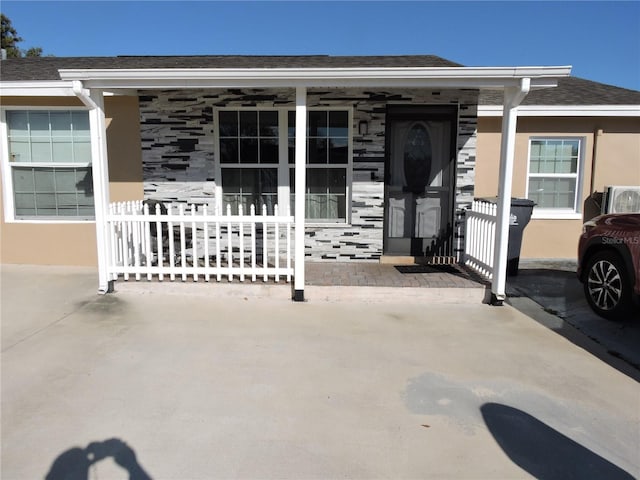 view of exterior entry with a porch, a shingled roof, and stucco siding