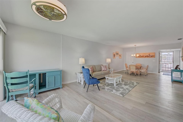 living room with a notable chandelier, visible vents, baseboards, and wood finished floors