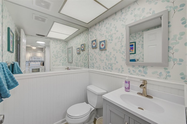 bathroom featuring visible vents, wainscoting, wallpapered walls, and toilet