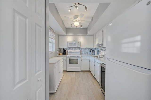 kitchen with backsplash, light countertops, white cabinets, white appliances, and a sink