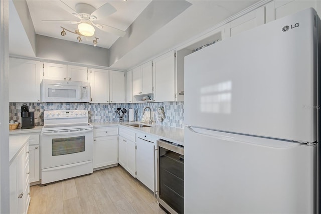 kitchen featuring beverage cooler, a sink, tasteful backsplash, white appliances, and light wood-style floors