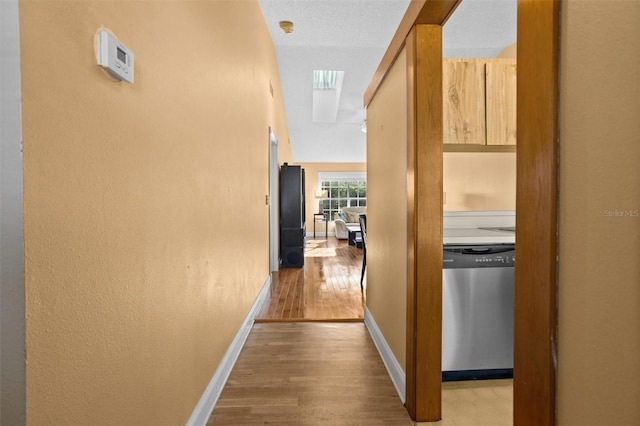 hallway featuring a skylight, baseboards, and light wood-style flooring