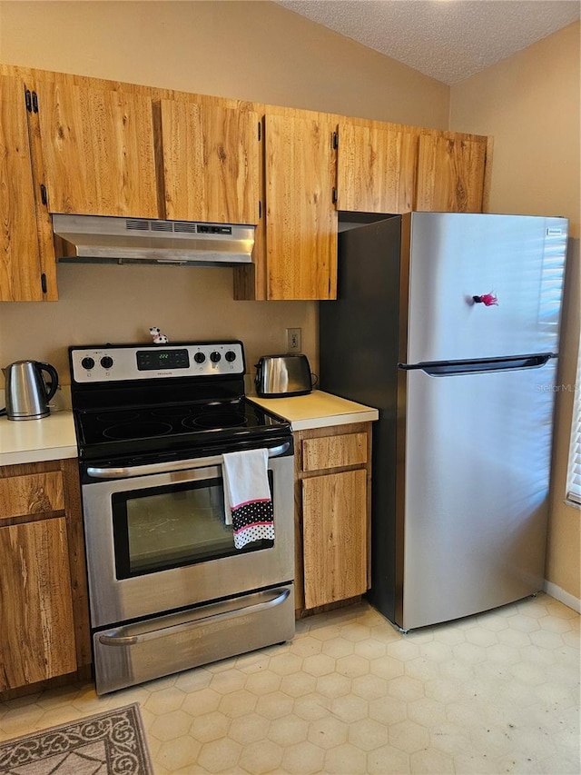 kitchen featuring under cabinet range hood, a textured ceiling, appliances with stainless steel finishes, brown cabinetry, and light countertops