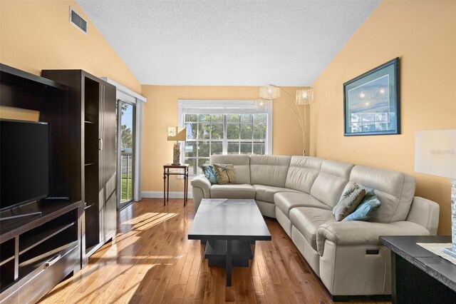 living room with visible vents, baseboards, vaulted ceiling, hardwood / wood-style flooring, and a textured ceiling