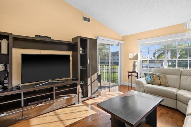 living room featuring visible vents, a textured ceiling, wood finished floors, baseboards, and lofted ceiling