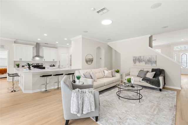 living area featuring arched walkways, recessed lighting, visible vents, light wood-type flooring, and crown molding