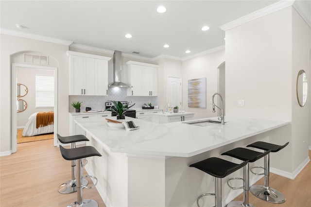 kitchen with a breakfast bar, a sink, visible vents, electric stove, and wall chimney exhaust hood