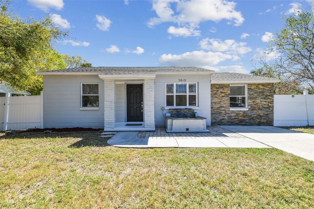 view of front of home featuring a patio, stone siding, a front yard, and fence