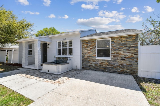 view of front of house with stone siding, fence, and a patio