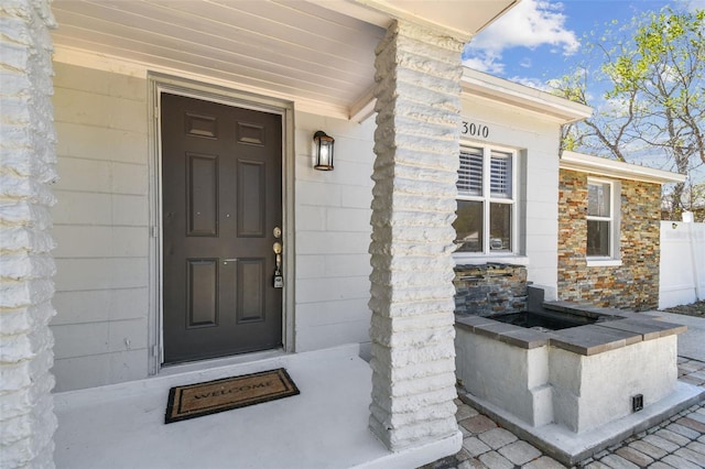 view of exterior entry with stone siding and fence