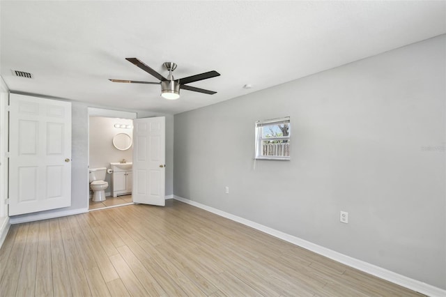 unfurnished bedroom featuring ceiling fan, light wood-style flooring, visible vents, baseboards, and ensuite bath