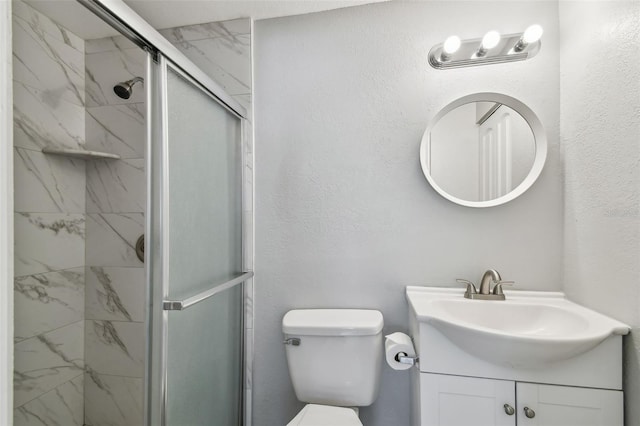 bathroom with a textured wall, toilet, vanity, and a marble finish shower