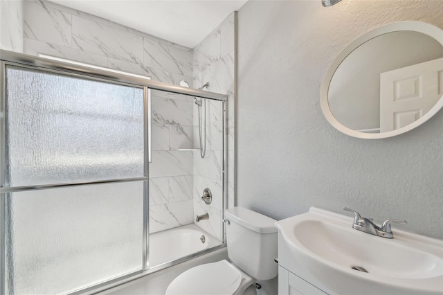 bathroom with toilet, shower / bath combination with glass door, vanity, and a textured wall