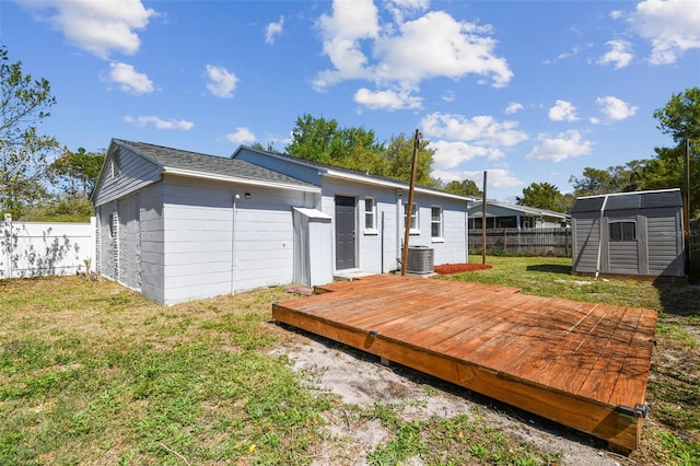 back of property with a storage shed, a wooden deck, a lawn, a fenced backyard, and an outdoor structure