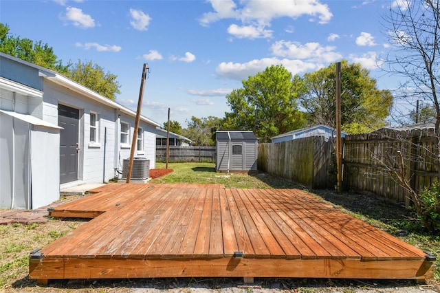 deck with an outbuilding, a lawn, central AC unit, a shed, and a fenced backyard