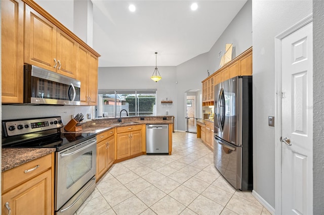 kitchen featuring arched walkways, stainless steel appliances, a sink, dark stone countertops, and a peninsula