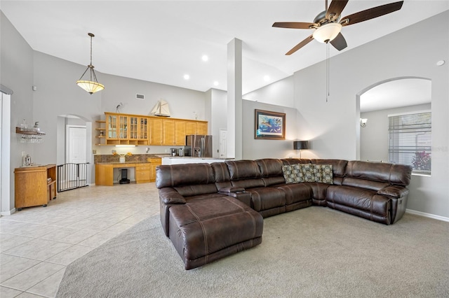 living room featuring arched walkways, light tile patterned floors, a towering ceiling, ceiling fan, and baseboards