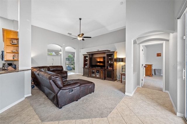 living room featuring arched walkways, ceiling fan, light tile patterned flooring, and a towering ceiling