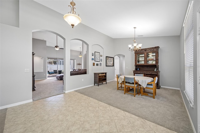 carpeted dining space featuring arched walkways, a high ceiling, tile patterned flooring, baseboards, and ceiling fan with notable chandelier