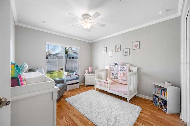 bedroom with light wood-type flooring, a nursery area, baseboards, and ornamental molding