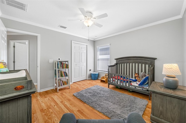 bedroom with baseboards, wood finished floors, visible vents, and crown molding