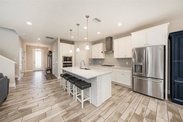 kitchen with a sink, appliances with stainless steel finishes, wall chimney range hood, and visible vents