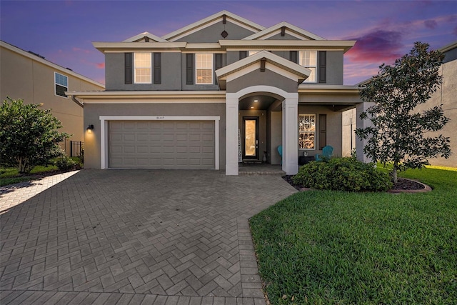 view of front of home with a garage, decorative driveway, a front lawn, and stucco siding