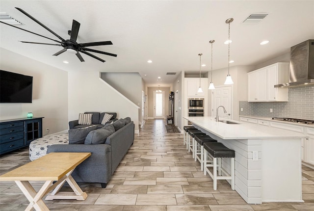 kitchen featuring stainless steel appliances, decorative backsplash, open floor plan, a sink, and wall chimney exhaust hood