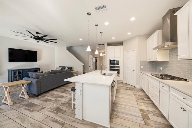 kitchen with tasteful backsplash, visible vents, appliances with stainless steel finishes, white cabinetry, and wall chimney exhaust hood