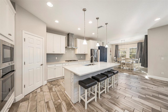 kitchen featuring a sink, wall chimney range hood, appliances with stainless steel finishes, decorative backsplash, and wood tiled floor