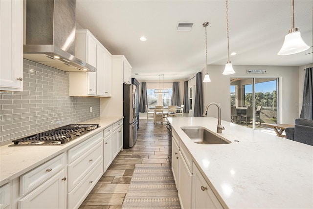 kitchen featuring visible vents, decorative backsplash, appliances with stainless steel finishes, a sink, and wall chimney exhaust hood