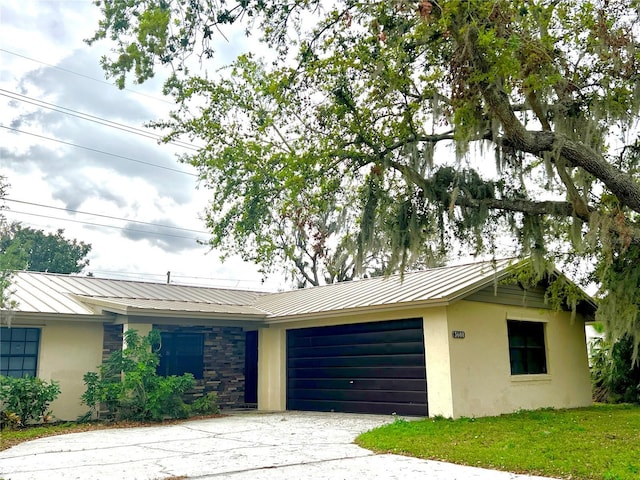 ranch-style home with a garage, stone siding, metal roof, a standing seam roof, and stucco siding