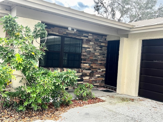 property entrance featuring a garage, stone siding, and stucco siding